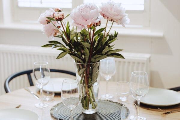 A laid table with pink flowers in a vase.