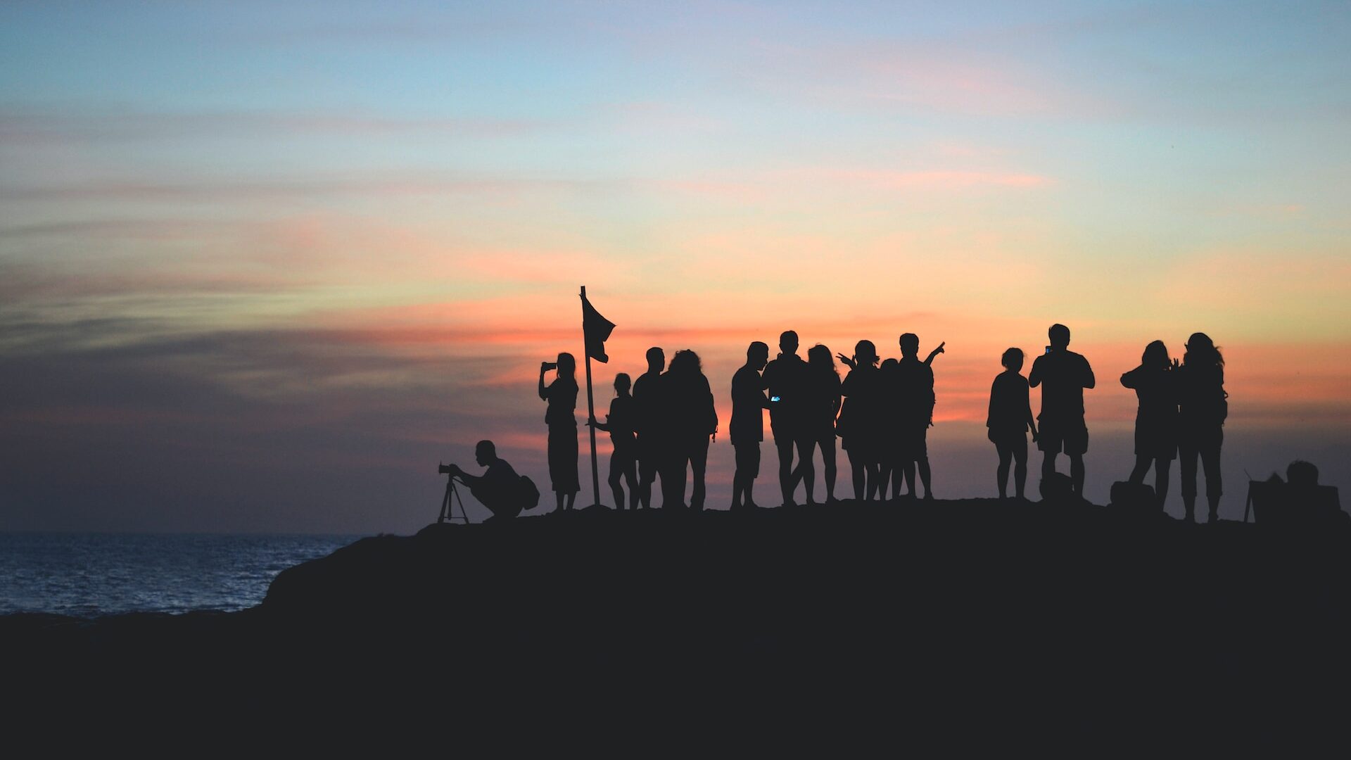 A group of people stood together overlooking the sea at dusk.