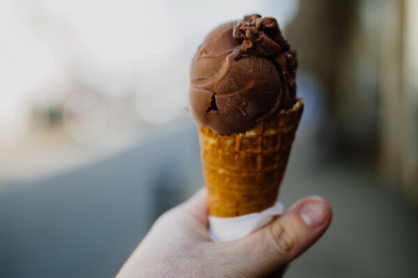 A man's hand holding a chocolate icecream cone.